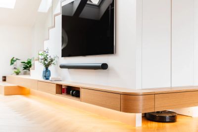 Detail TV stěny s dubovou odkládací skříňkou, soundbarem a robotickým vysavačem