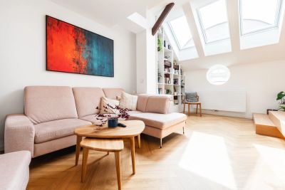Obývací pokoj — růžová sedačka, barevný obraz a knihovna pod šikminou se střešními okny